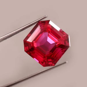 以下が含まれることがあります： 銀色のピンセットで保持された、ファセット加工された正方形カットのルビーの宝石。 ルビーは深く飽和した赤色で、光を反射する複数のファセットがあります。 宝石はニュートラルな背景に対して焦点となっています。