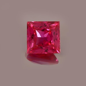 May include: A square-cut gemstone with a vibrant, saturated pinkish-red color. The stone features a faceted surface that creates sharp geometric reflections and internal light refraction, showcasing a clear, transparent quality throughout the piece.