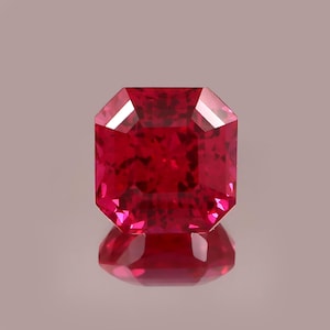 Könnte beinhalten: Ein facettierter, quadratisch geschliffener Rubin. Der Edelstein hat eine tiefe, lebendige rote Farbe und eine reflektierende Oberfläche. Der Rubin liegt auf einer spiegelnden Oberfläche.