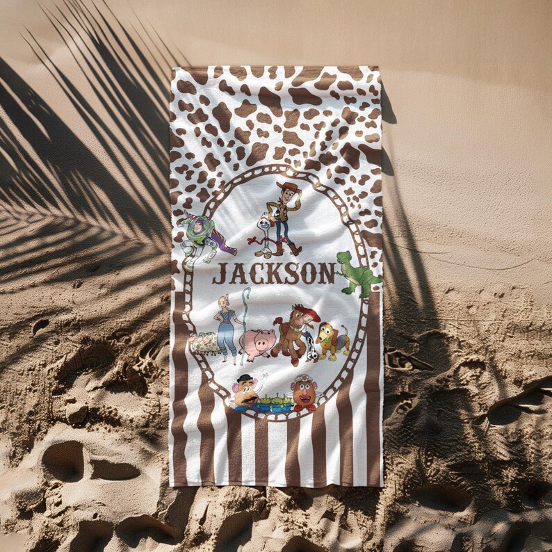 May include: A rectangular beach towel featuring a brown and white cowhide pattern at the top and brown and white stripes at the bottom. The center has a circular design with cartoon characters and the name "Jackson".
