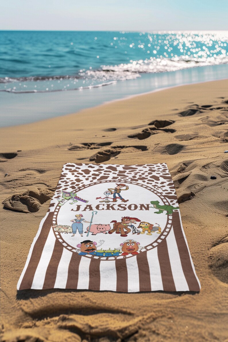 May include: A personalized beach towel with a brown and white cowhide pattern border and vertical brown stripes. The center features a circular design with cartoon characters and the name "JACKSON" in green letters.