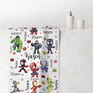 Pu&ograve; includere: Asciugamano da bagno bianco con personaggi di supereroi dei cartoni animati e il nome "Kasen" ripetuto. L'asciugamano presenta personaggi come Spider-Man e Hulk, con dettagli rossi, blu e gialli. L'asciugamano &egrave; mostrato in un bagno.