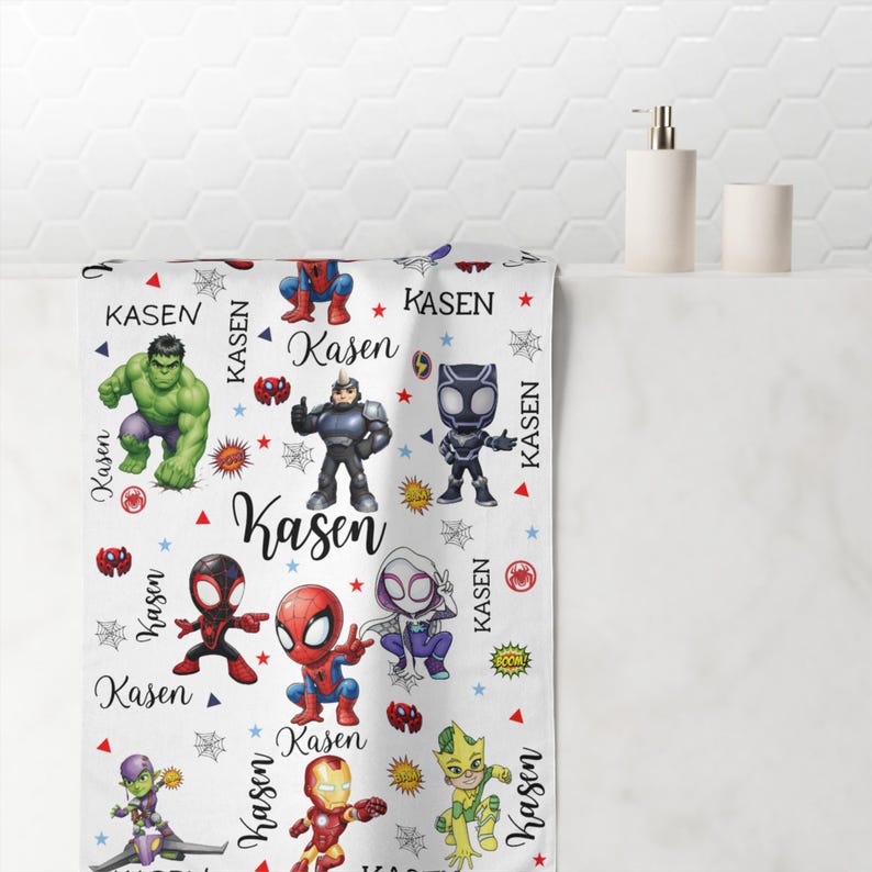 Pu&ograve; includere: Asciugamano da bagno bianco con personaggi di supereroi dei cartoni animati e il nome "Kasen" ripetuto. L'asciugamano presenta personaggi come Spider-Man e Hulk, con dettagli rossi, blu e gialli. L'asciugamano &egrave; mostrato in un bagno.