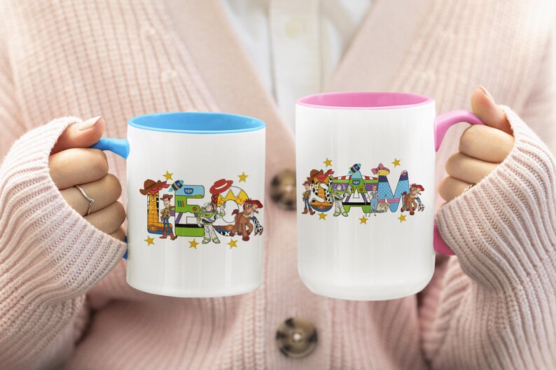Puede incluir: Dos tazas de cer&aacute;mica blanca con dise&ntilde;os coloridos. Una taza tiene el interior y el asa azules, la otra tiene el interior y el asa rosas. Las tazas presentan la palabra "TEAM" con personajes de dibujos animados y estrellas.