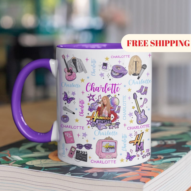 K&ouml;nnte beinhalten: Wei&szlig;er Keramikbecher mit lila Innenraum und Henkel. Der Becher ist mit einer Collage von Musik- und Unterhaltungsgrafiken dekoriert, darunter Gitarren, Mikrofone und der Name "Charlotte". Der Becher hat den Text "Hannah Montana" darauf.
