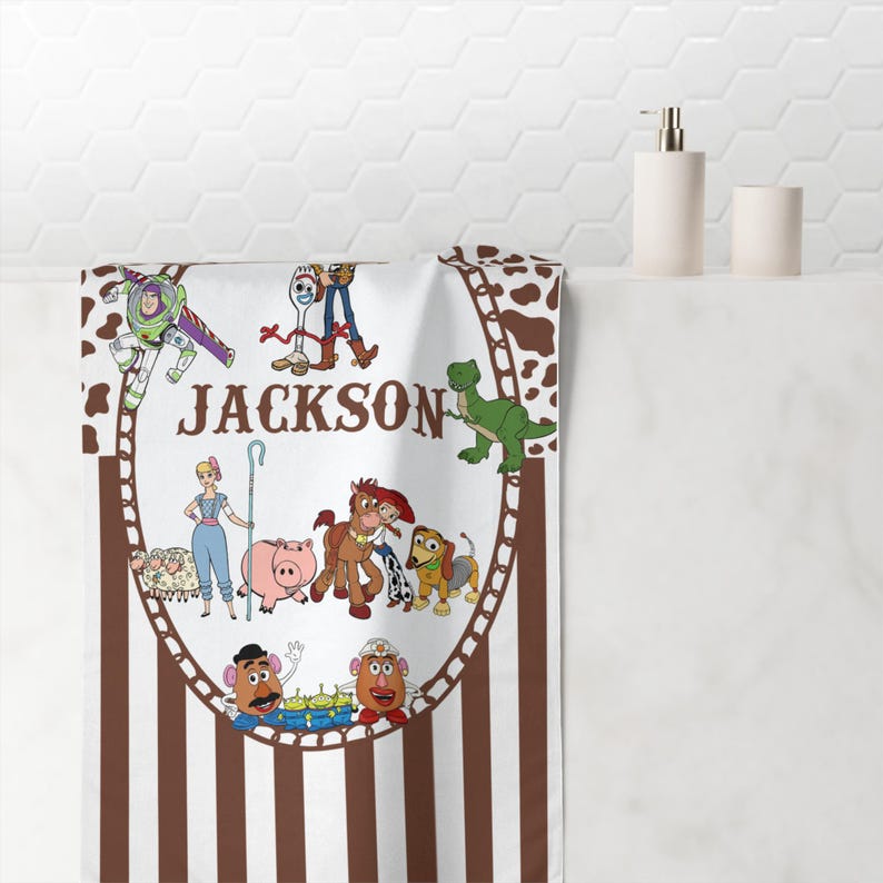May include: White and brown striped bath towel featuring a cartoon illustration of characters from the Toy Story movie. The name "JACKSON" is printed in the center of the towel.