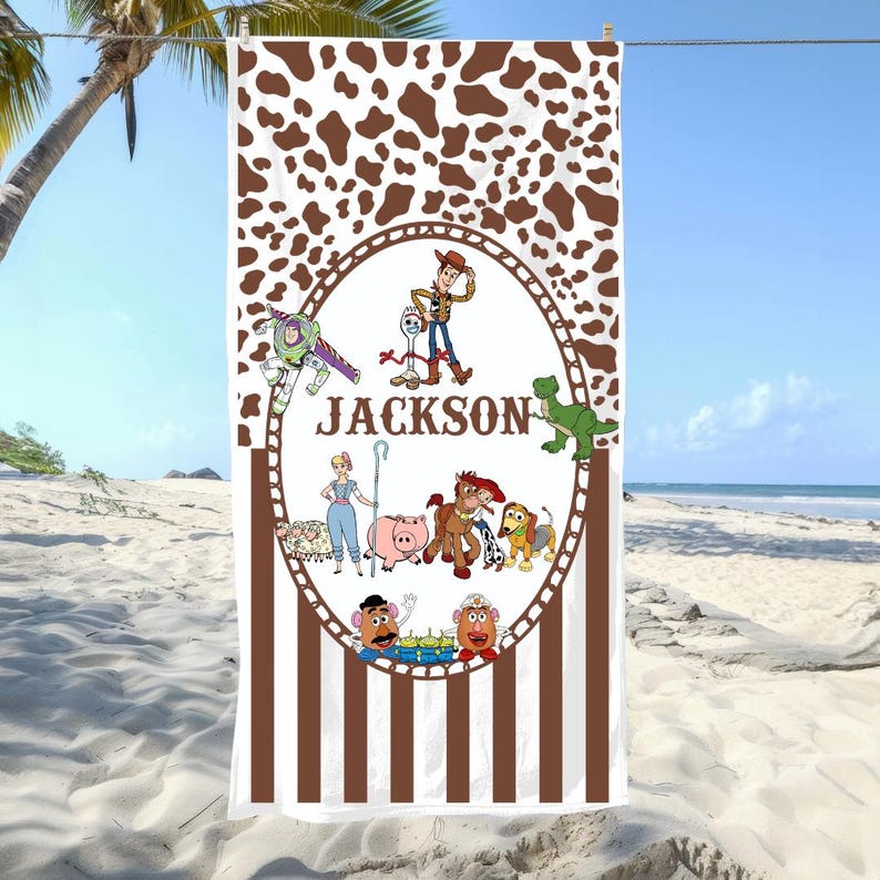 May include: A white beach towel with a brown cow-print top and vertical brown and white stripes at the bottom. The center features a cartoon design with the name "JACKSON" and various character illustrations.