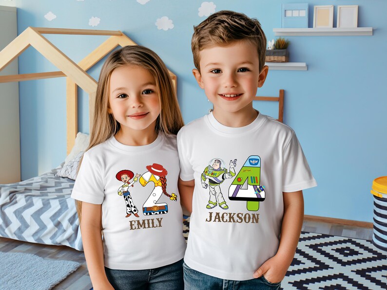 以下が含まれることがあります： 白いTシャツを着た2人の子供たち。1つのシャツには、数字の2と「Emily」という名前が付いたウッディとジェシーのデザインが施されています。もう1つのシャツには、数字の4と「Jackson」という名前が付いたバズ・ライトイヤーのデザインが施されています。