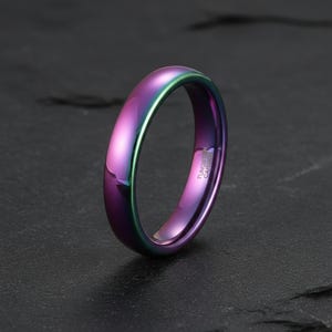 Op de afbeelding: Een iriserende ring met een gepolijste afwerking, die een spectrum aan kleuren weergeeft, van paars tot groen en blauw. De binnenkant van de ring is gegraveerd met de woorden "Tungsten Carbide".