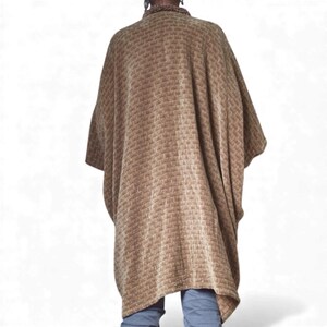 May include: A brown, textured poncho with a woven pattern. The poncho is draped over the shoulders and has wide sleeves. The garment is a warm, neutral color and appears to be made of a soft material.