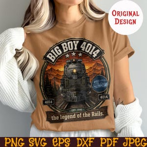 May include: A tan t-shirt featuring a detailed graphic of a steam train, labeled "Big Boy 4014" with the text "the legend of the Rails." The design includes mountains and trees, with the words "Original Design."