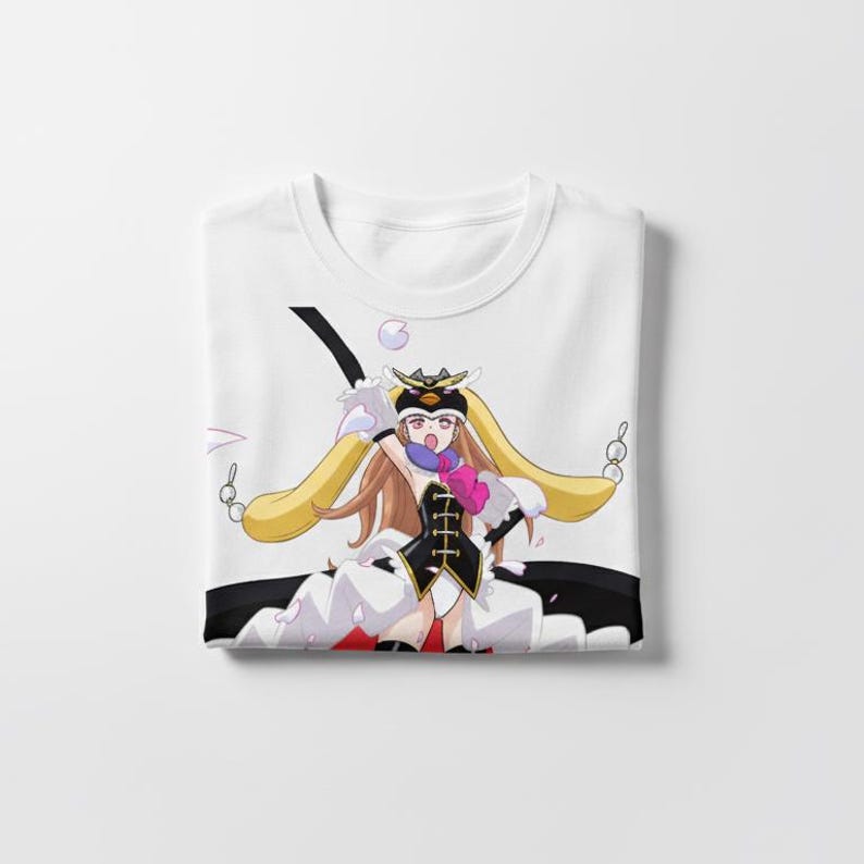 May include: White t-shirt featuring a colorful anime-style illustration. The design includes a character with long blonde hair, a black and white outfit, and a pink heart-shaped detail. The shirt is folded neatly.