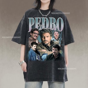 May include: Dark gray t-shirt featuring a graphic of Pedro Pascal with the name "PEDRO" in large letters above his image. The shirt has a vintage, distressed look, with multiple images of the actor. The brand name "NOLIMITFASHIONS" is printed on the shirt.