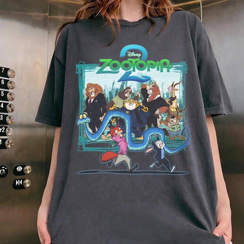 May include: Dark grey t-shirt with a colourful graphic from the Disney film Zootopia. The design features animal characters, the movie title, and the Disney logo. The shirt has short sleeves and a relaxed fit.