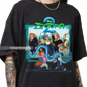 May include: Black t-shirt with a vibrant graphic from Disney's Zootopia 2. The design showcases animal characters and the film's title in teal and green. The tee has a crew neck and short sleeves.