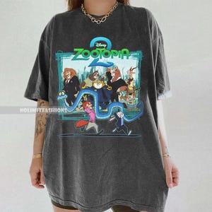 May include: Dark grey t-shirt with a colourful graphic from the Disney film Zootopia. The graphic features the film's title and various animal characters. The shirt has a relaxed fit and short sleeves.