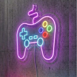 May include: A neon sign shaped like a video game controller, with a purple outline and colorful buttons. The controller is mounted on a gray concrete wall. The buttons are in the colors of red, yellow, green, and blue.