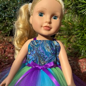 May include: A doll wearing a blue and green marbled print dress with a purple tulle skirt and a purple satin bow.