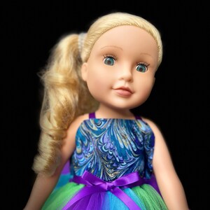 May include: A doll with blonde hair wearing a blue and gold patterned dress with a purple tulle skirt and a purple satin bow.