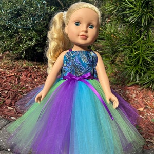May include: A doll wearing a teal, purple, and green tulle dress with a purple ribbon. The doll has blonde hair and blue eyes.