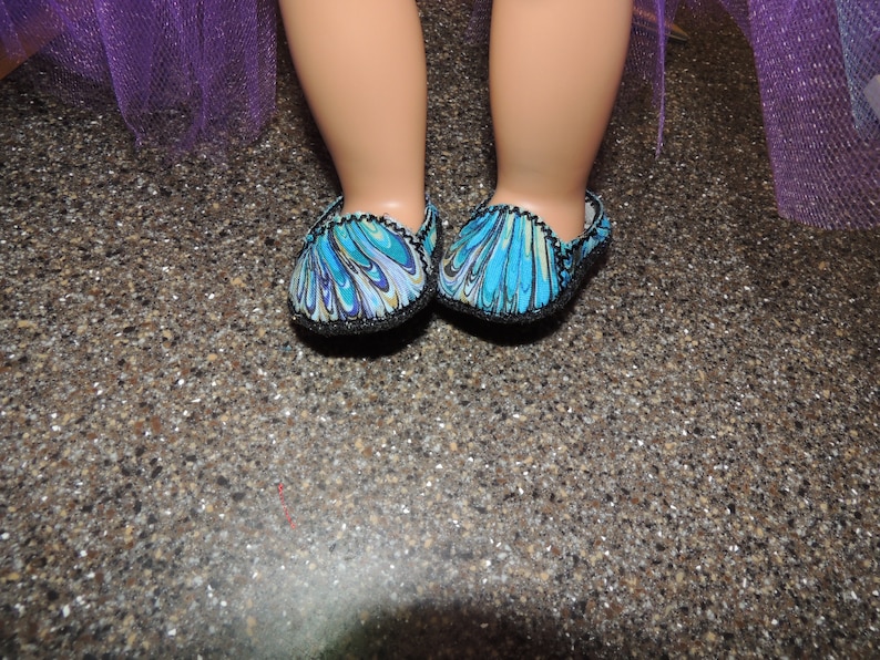 May include: A pair of blue and green patterned slippers with black trim. The slippers have a swirl design.