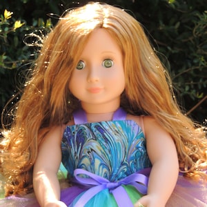 May include: A doll with long, curly, light brown hair wearing a blue and gold patterned dress with a purple ribbon. The doll is wearing a multi-colored tulle skirt.