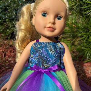 May include: A doll with blonde hair wearing a blue and gold marbled sleeveless top and a multi-colored tulle skirt with a purple satin ribbon.