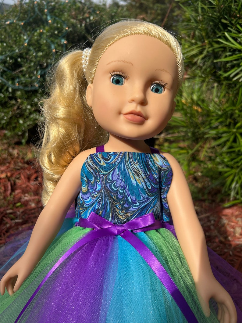 May include: A doll with blonde hair wearing a blue and gold marbled sleeveless top and a multi-colored tulle skirt with a purple satin ribbon.