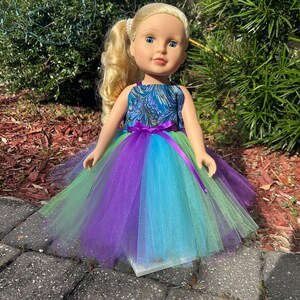 May include: A doll wearing a blue and green patterned dress with a purple tulle skirt. The doll has blonde hair and blue eyes.