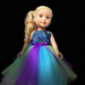 May include: A blonde doll wearing a blue and green patterned dress with a purple and blue tulle skirt.