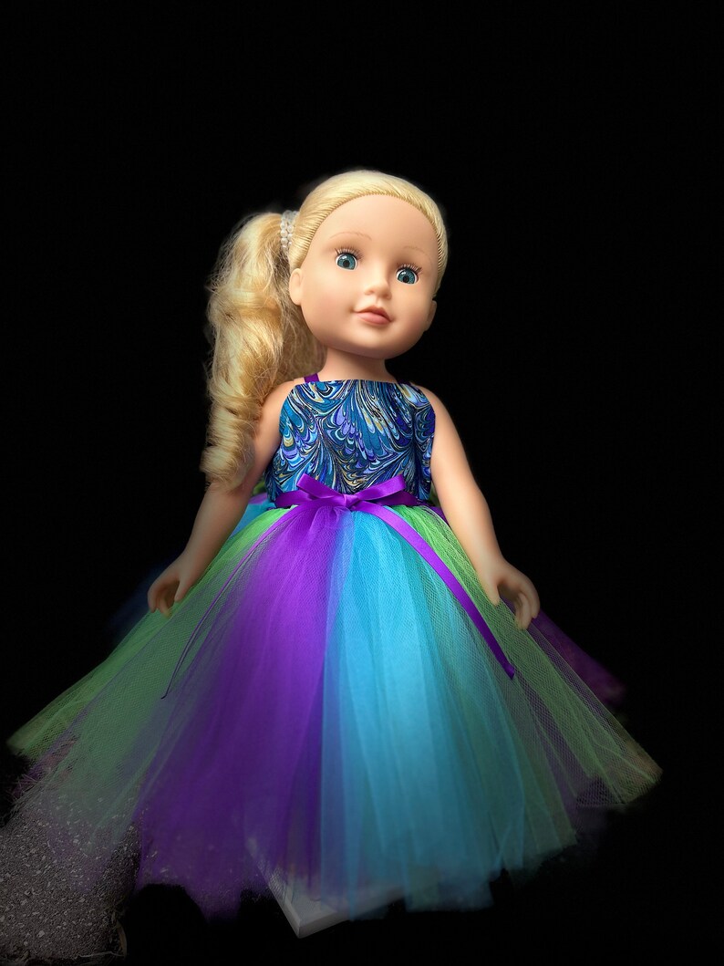 May include: A blonde doll wearing a blue and green patterned dress with a purple and blue tulle skirt.