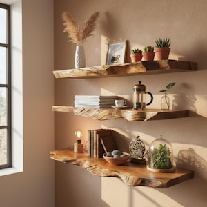 Op de afbeelding: Drie zwevende houten planken met een natuurlijke rand. De planken zijn versierd met decoratieve items, waaronder planten in terracotta potten, boeken, een cafetière, een lamp en een glazen stolp met groen.