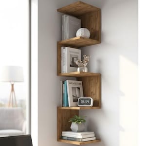 Puede incluir: Estantería esquinera de madera con diseño en zigzag, montada en una pared blanca. Las estanterías exhiben libros, objetos decorativos y una pequeña planta. Un reloj digital muestra la hora 18:54. La unidad es de madera con veta natural.
