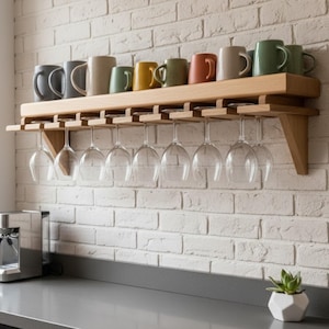 Può includere: Un portabicchieri e tazze a parete in legno. Il portabicchieri contiene bicchieri da vino trasparenti e una varietà di tazze colorate. Il portabicchieri è montato su un muro di mattoni bianchi sopra un piano di lavoro grigio.