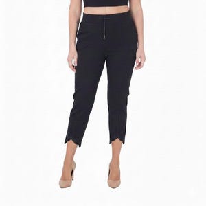 May include: A woman in a black crop top and trousers. The trousers have a scalloped hem. She is also wearing nude heels. The outfit is all black.