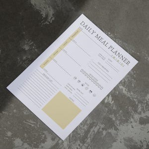 May include: A white Daily Meal Planner sheet with black and light yellow text and design elements. The planner includes sections for meals, water intake, mood, workout, and a grocery list. The text includes "DAILY MEAL PLANNER" and "GROCERY LIST".