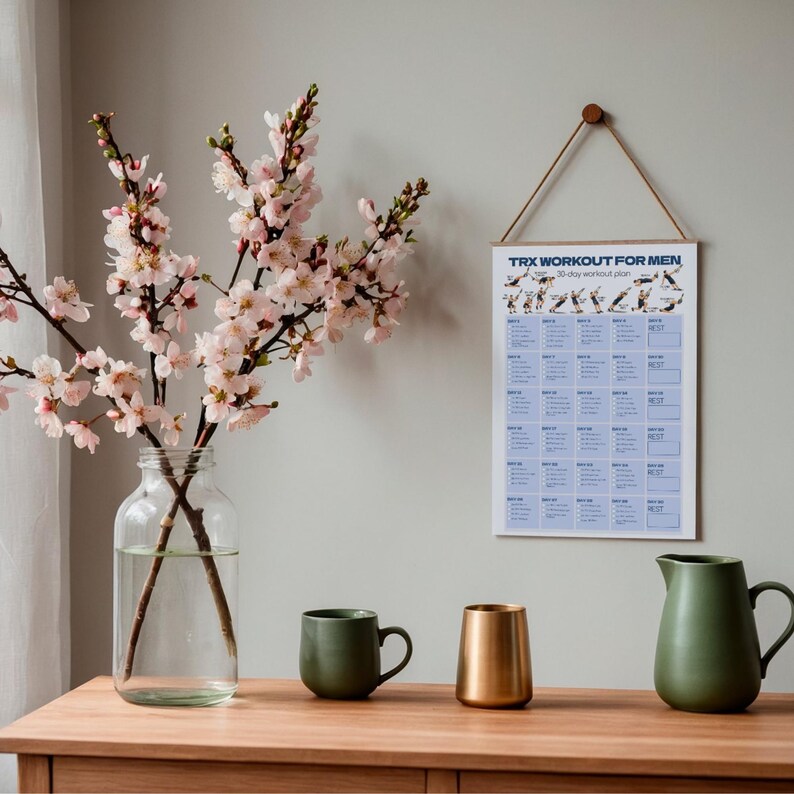 May include: A clear glass vase with pink cherry blossom branches, a wall-mounted TRX workout plan chart, a matte green mug, a metallic gold tumbler, and a matte green pitcher. The chart features the text TRX WORKOUT FOR MEN 30-day workout plan.