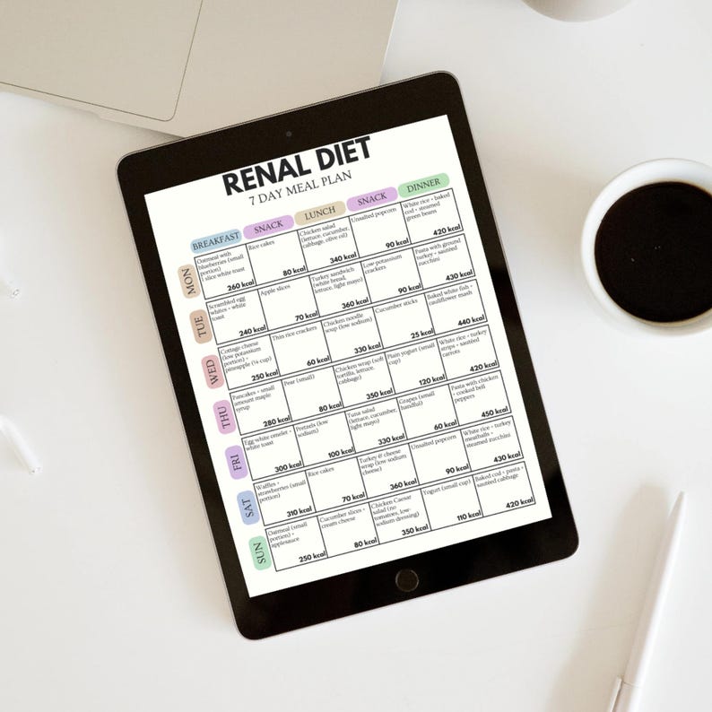 Puede incluir: Una tableta negra muestra un "RENAL DIET 7 DAY MEAL PLAN" con sugerencias de comidas diarias. El plan incluye opciones para desayuno, merienda, almuerzo, merienda y cena. Una taza de caf&eacute; y un bol&iacute;grafo est&aacute;n sobre la superficie blanca.
