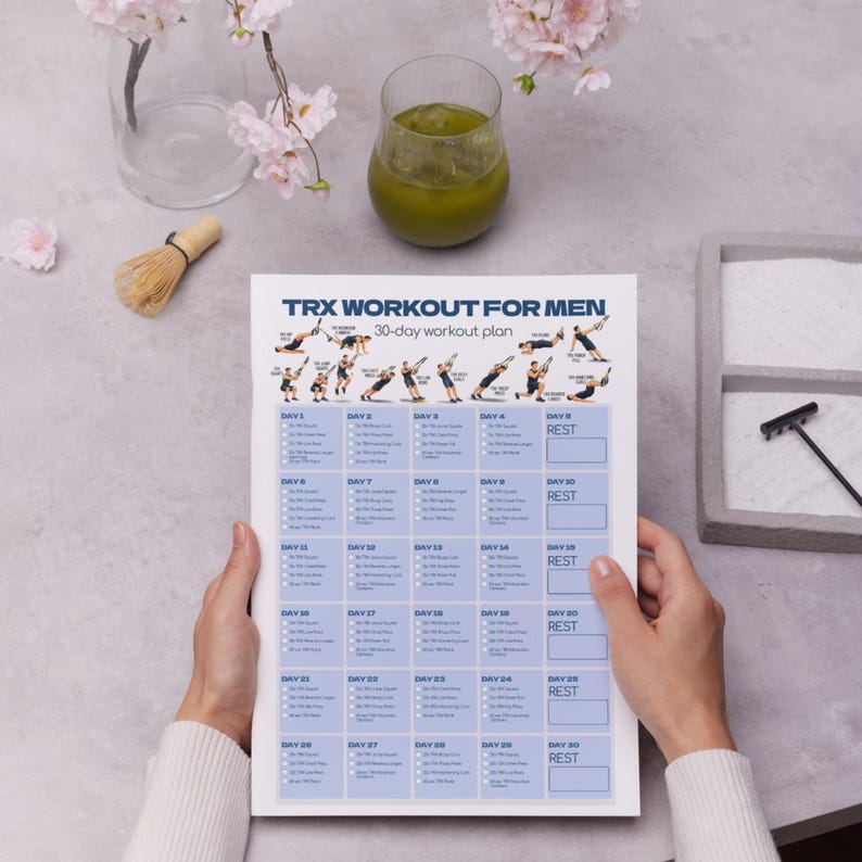 May include: A white paper sheet featuring a 30-day TRX workout plan with blue text and grid boxes. The header reads TRX WORKOUT FOR MEN and includes small illustrations of various suspension training exercises performed with straps and handles.