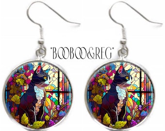 May include: A pair of round silver-toned drop earrings featuring a colorful stained glass-style illustration of a black and white cat sitting near a window. The text *BOOBOO&REG* is printed in black above the circular earring pendants.