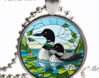 May include: Silver-toned pendant necklace featuring a round charm with a stained-glass style illustration of two loons on a lake. The loons have black heads, white bodies, and green accents. The charm includes the text "BOOB&REG".