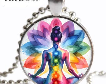 May include: A silver-toned pendant necklace featuring a circular glass cabochon with a colorful illustration of a person in a seated meditation pose. The figure displays seven glowing chakra points along the spine against a vibrant lotus flower background.
