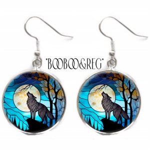 May include: A pair of silver dangle earrings with a round blue and yellow stained glass design featuring a wolf howling at the moon. The design is surrounded by a silver frame.