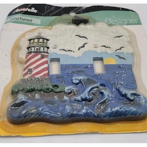 May include: A hand-painted Amerelle Designer Collection double toggle light switch plate featuring a red and white striped lighthouse on a rocky shore, a blue ocean with crashing waves, a yellow sun, and black birds flying in a white sky.