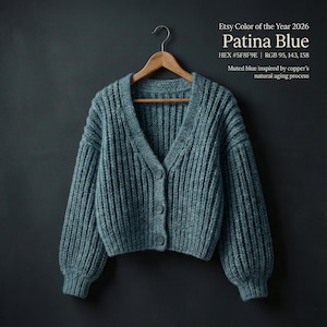 May include: A Patina Blue, chunky knit cardigan with a V-neck and three buttons, hanging on a wooden hanger. The color is described as muted blue, inspired by copper's natural aging process. The text on the image says "Etsy Color of the Year 2026".