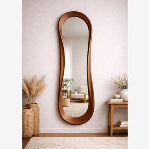 以下が含まれることがあります： 木製のフレームが付いた、細長い形状の大きな鏡。 鏡は白い壁に取り付けられており、ニュートラルな色調と自然な要素のある部屋を映し出しています。 フレームは温かみのある茶色の仕上がりです。 鏡の高さは約180cmです。