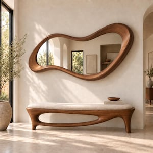 May include: A large, wall-mounted mirror with an irregular, organic wooden frame featuring a smooth, flowing shape. Below the mirror sits a long, low wooden bench with a cream-coloured upholstered seat and a hollow, curved base design.