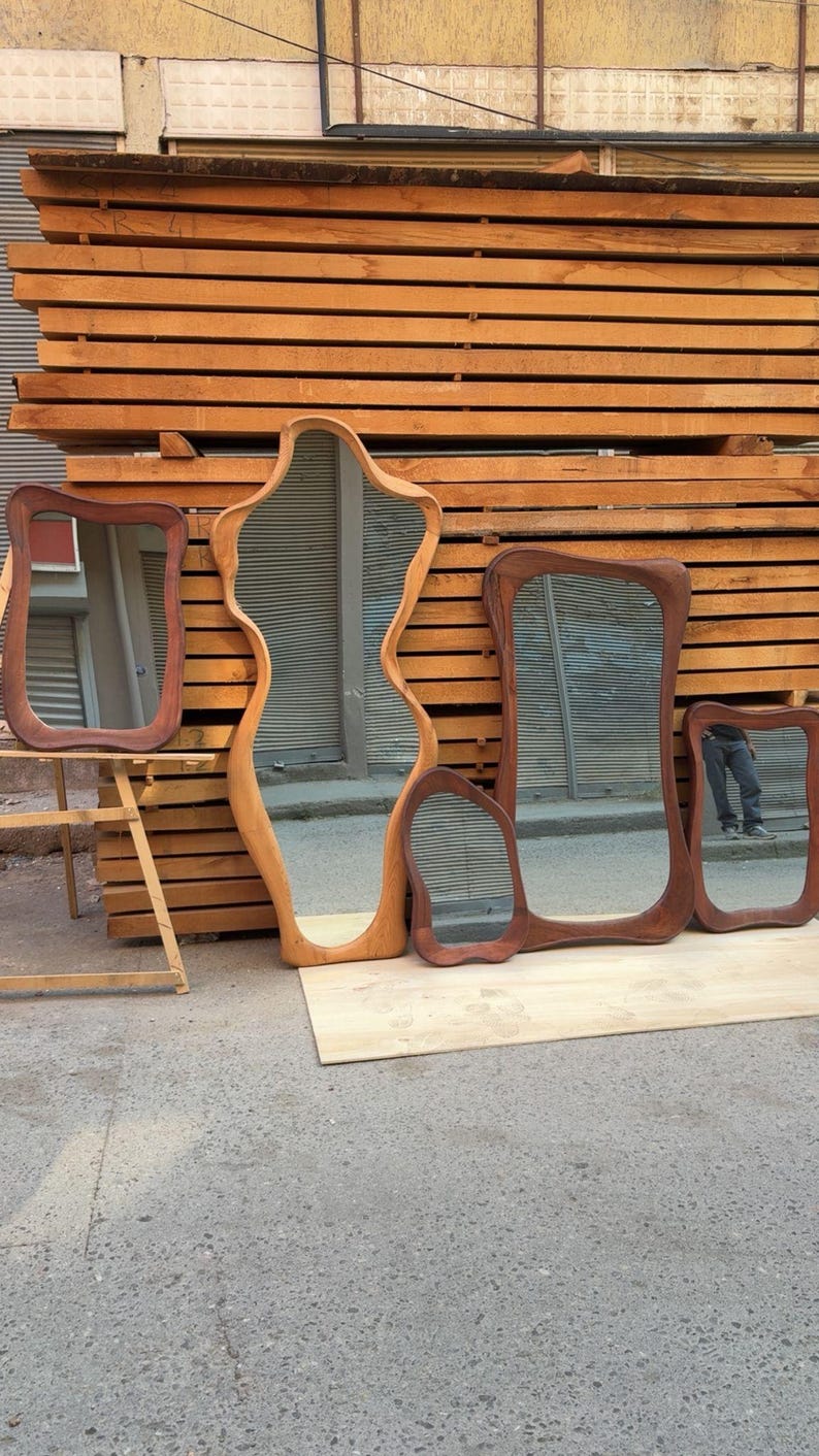 Puede incluir: Una colecci&oacute;n de cuatro espejos de madera con formas org&aacute;nicas irregulares y marcos curvos y lisos. Los espejos var&iacute;an en tama&ntilde;o y tono de madera, desde marr&oacute;n claro a oscuro, y se muestran apoyados contra una pila de madera.