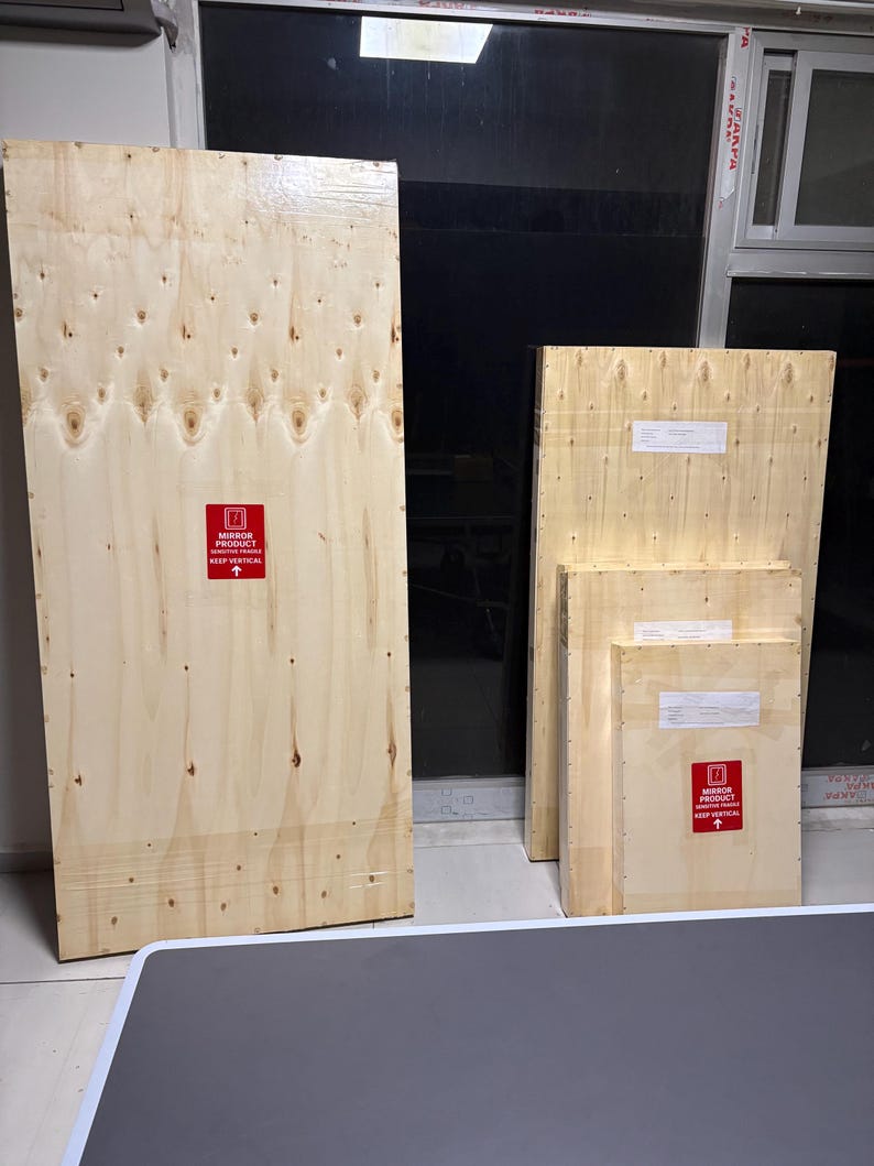 May include: Four rectangular wooden shipping crates of varying sizes, each featuring a light tan wood grain finish. The crates display red warning labels that read MIRROR PRODUCT SENSITIVE FRAGILE KEEP VERTICAL with an upward pointing arrow.