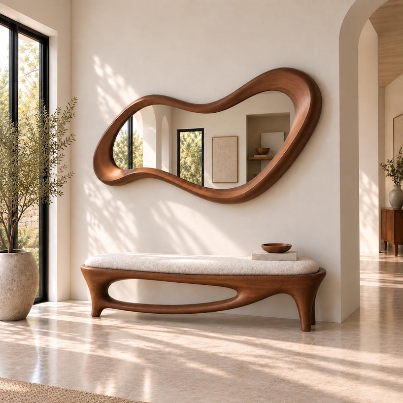 May include: A large, organic-shaped wall mirror with a thick, smooth, dark wood frame. Below it sits a matching wooden bench featuring a long, curved base and a thick, cream-coloured upholstered seat cushion, creating a cohesive furniture set.
